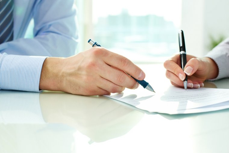zwei Hände mit Stiften bei Vertragsunterzeichnung
